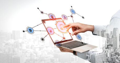 A professional hand interacts with a laptop showing digital icons symbolizing data sharing and connectivity against a modern city backdrop, reflecting innovation. Tessel