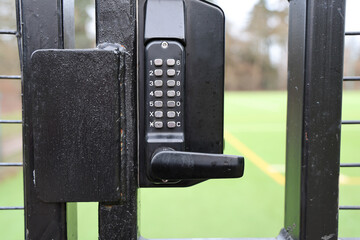 Close-Up of Black Gate Lock with Keypad on Sports Field Fence