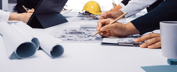 Group of professionals engaged in a collaborative meeting, reviewing blueprints and documents while brainstorming ideas in a contemporary office setting. SACTR