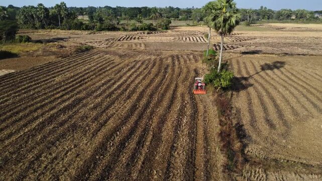 Aerial view of an indian tractor plowing field in odisha, India. Cinematic look of farming technology and the agriculture start after the harvest season.