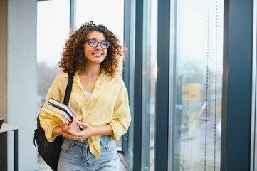 Smiling student carrying books arriving at university building