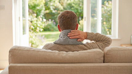 Man using heating pad on neck while sitting on couch at home