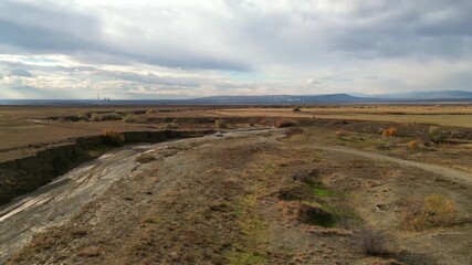 Aerial shot of a white off-road vehicle navigating a rugged, dry river channel in the rural valleys of Georgia. Cinematic drone footage capturing adventure travel in the Caucasus region during autumn.