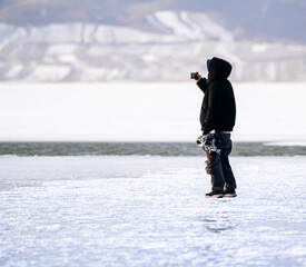 person photographing in the snow on a half frozen lake with water and ice