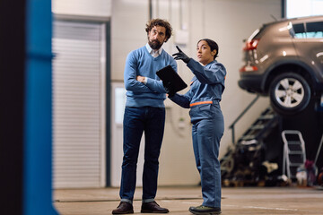 Fototapeta premium Female auto repair shop worker communicating with customer in garage.