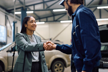 Obraz premium Happy woman shaking hands with mechanic in auto repair shop.