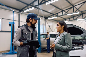 Fototapeta premium Auto repairman talking to female customer in workshop.