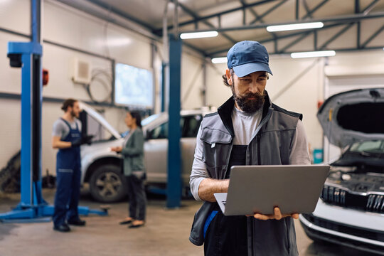 Mature mechanic working on laptop in auto repair shop.