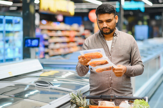 Man choosing frozen fish in supermarket freezer aisle