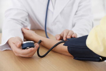 Doctor checking woman's blood pressure with sphygmomanometer at table in hospital, closeup