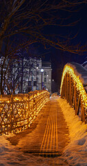 Fototapeta premium Pedestrian bridge decorated with festive lights during a snowy winter night, creating a cozy and atmospheric urban walkway.