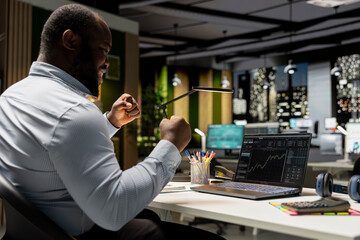 Pleased black man celebrating global market trends going up, feeling happy and joyful with the cryptocurrency success and making money. Business development goals after hours.