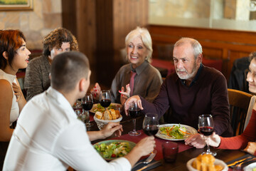 Multi-generation family discussing daily life while having fresh food and wine in restaurant