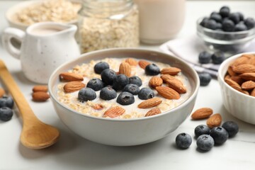 Tasty oatmeal with almond milk, nuts and blueberries on white marble table, closeup