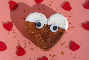 Creative flat lay with funny joke eyes on Delicious fresh croissant topped with colorful flavor Ganache. Creation unique heart shape bakery. Puff pastry holiday love gift present idea Valentine's day