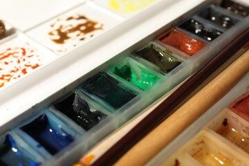 Palette with watercolor paints and brushes as background, closeup
