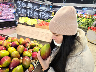 Fototapeta premium A young woman selects vegetables and avocados in the produce section of a supermarket.