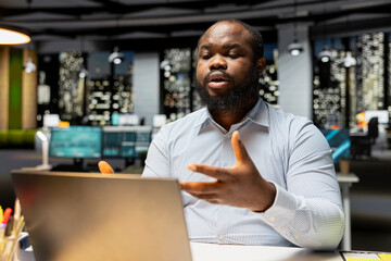 Obraz premium African american man participates in web video call meeting to share insight with associates, speaking confidently about business matters into the microphone. Professional networking.