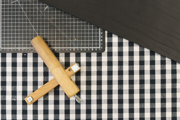 Top view of a wooden marking gauge on a checkered fabric next to a cutting mat and dark wood panel.