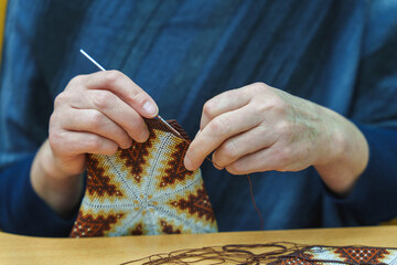 Hands of a woman bead crocheting a colorful geometric pattern.