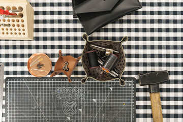 Leather crafting tools and handmade goods on a checkered workbench.