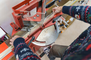 A craftsman uses a red miter guillotine to cut precise angles on wooden picture frame molding.