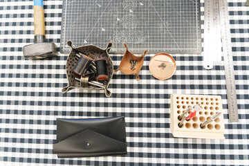 Leather crafting tools and handmade goods on a checkered workbench.