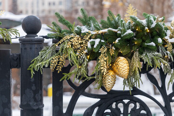 Detailed view of golden pine cones and evergreen branches with fairy lights on a decorative fence in Moscow, Russia.
​
