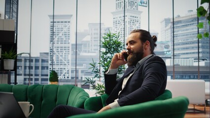 CEO multitasking and managing an important phone call with investors while he reviews financial reports on his laptop. Strategic decision making in corporate life at the workplace. Camera A.