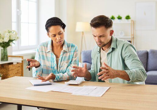Stressed diverse mixed race couple reviews household bills and monthly expenses, using a calculator to track debt and finance, getting confused about strange figures and numbers in the account balance