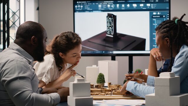 Real estate professionals engage in meeting to review blueprints and 3D models, planning for a large scale urban development project aimed at housing and infrastructure growth. - Powered by Adobe