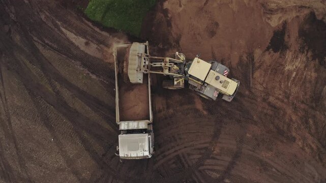 Top-Down Drone View of Wheel Loader Loading Soil into Dump Truck at Construction Site