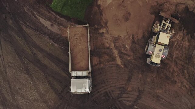 Top-Down Drone View of Wheel Loader Loading Soil into Dump Truck at Construction Site