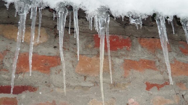 Icicles dangle from snow-covered rooftop. Glistening forms contrasting with rustic charm of old brick wall. Witness winter beauty and delicate balance of nature. Freezing of dripping or flowing water