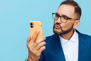 A focused business man checks a mobile device against a bold blue background, projecting professionalism, calm confidence, and thoughtful mood in a clean studio setting.