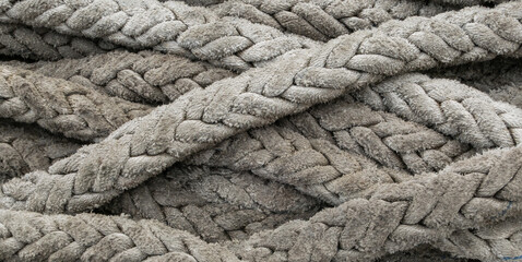 Close-up of thick, weathered nautical ropes with heavy braided texture. Grey industrial cordage ideal for maritime, strength, and tactile background concepts