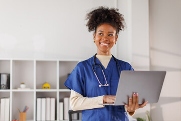 Medical professional in blue scrubs working on laptop, African american in afro hair smiling while...