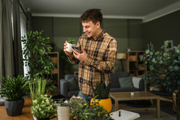 Young man using smart phone identifying succulent plant at home