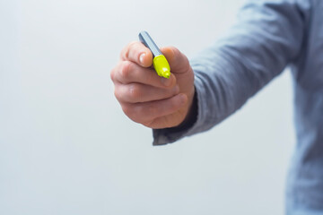 Fototapeta premium Close-up of a hand holding a bright green neon highlighter against a light background. Concept focuses on concentration, important notes, increased productivity and learning or work process.