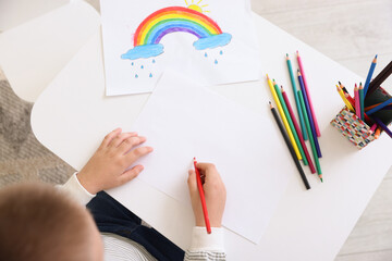 Little boy drawing with pencil at table indoors, top view