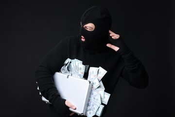 Masked thief with briefcase full of money on black background