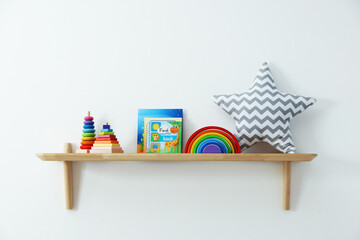 Shelf with different toys and books on light wall