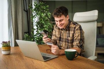 Young man doing online shopping with credit card holding smart phone