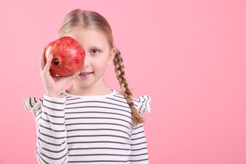 Little girl with ripe pomegranate on pink background. Space for text