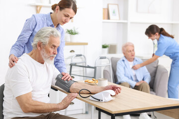 Fototapeta premium Caregiver measuring senior man's blood pressure at home