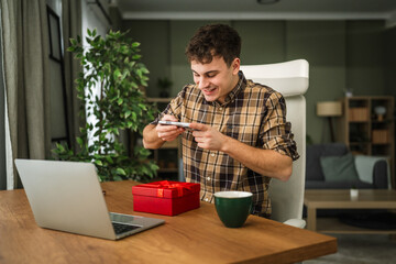 Young man photographing gift box unpacking with smart phone