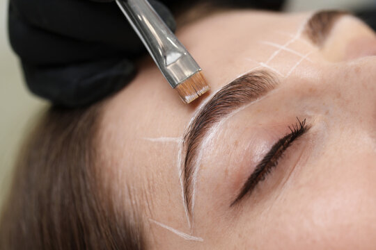 Beautician drawing marks on woman's face before permanent eyebrow makeup procedure, closeup