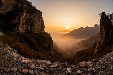 Sunrise over a misty mountain valley with rocky cliffs and forested slopes