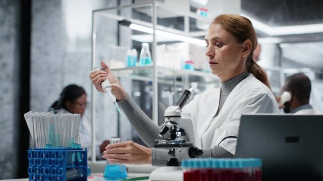 Researcher pipetting reactant into blue solution for purity analysis. Female cytotechnologist adding liquid agent to test tube to observe chemical reaction properties, camera B