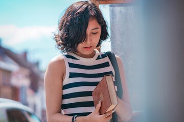 Young woman, take a book from a box of books on the street, she is standing on the sidewalk.